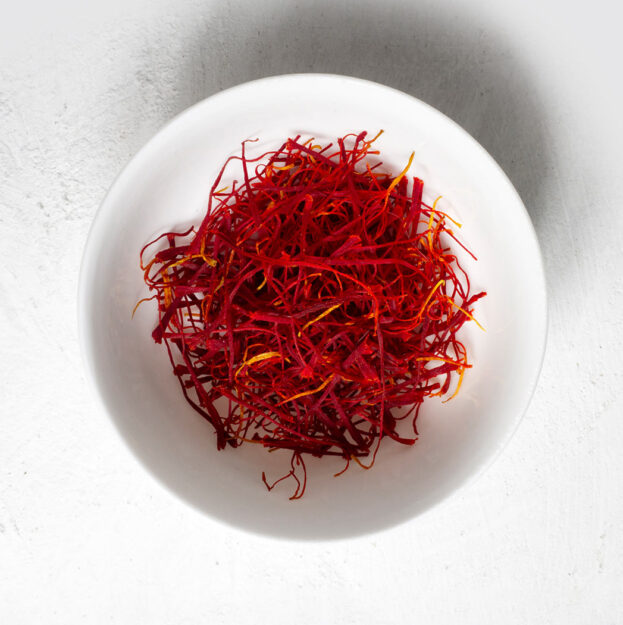 Premium Iranian Saffron threads in a decorative container, showcasing vibrant red color and high quality for culinary and medicinal use.